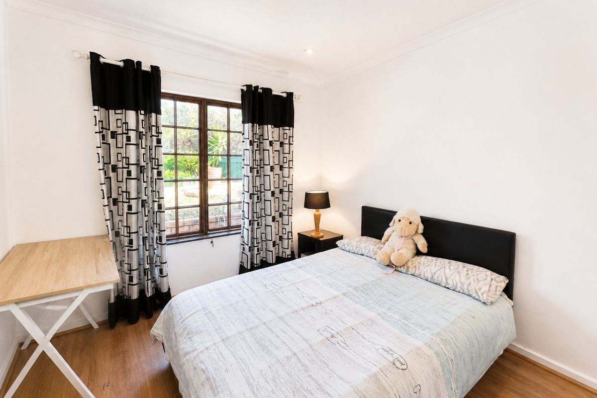 A well-maintained bedroom featuring laminate flooring, coved ceilings, and a timber-framed window overlooking the garden.