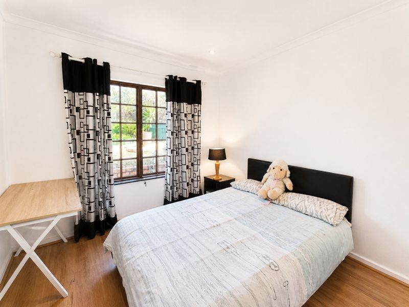 A well-maintained bedroom featuring laminate flooring, coved ceilings, and a timber-framed window overlooking the garden.