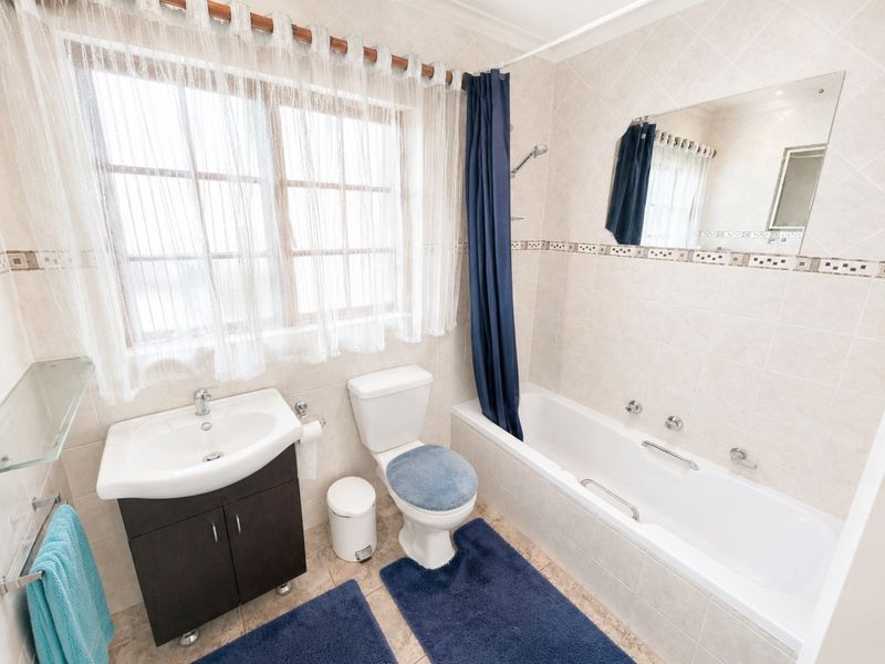 A functional bathroom featuring a vanity cabinet, a standard bathtub with shower mixer, and neutral wall tiling.