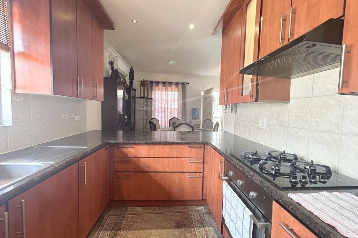 A functional kitchen featuring wood-finish cabinetry, granite countertops, a gas hob, and an integrated oven, flowing into an adjacent dining area.
