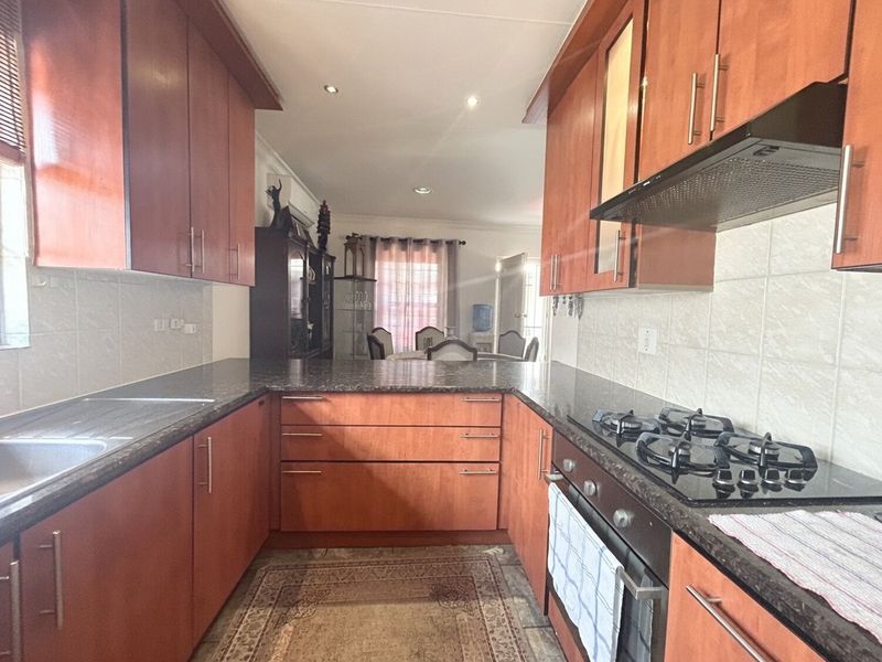 A functional kitchen featuring wood-finish cabinetry, granite countertops, a gas hob, and an integrated oven, flowing into an adjacent dining area.