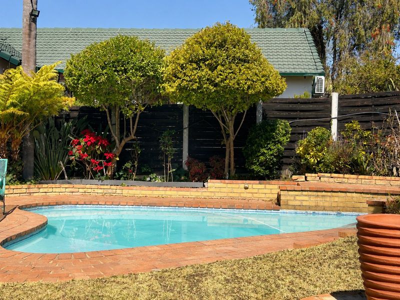 A private outdoor pool area featuring a brick-edged swimming pool, a low brick retaining wall, and established garden landscaping against a timber boundary fence.