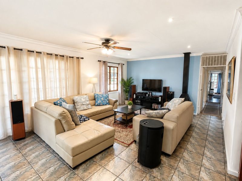 A spacious living room featuring tiled flooring, a ceiling fan, and a modern freestanding fireplace, creating a comfortable and functional family area.
