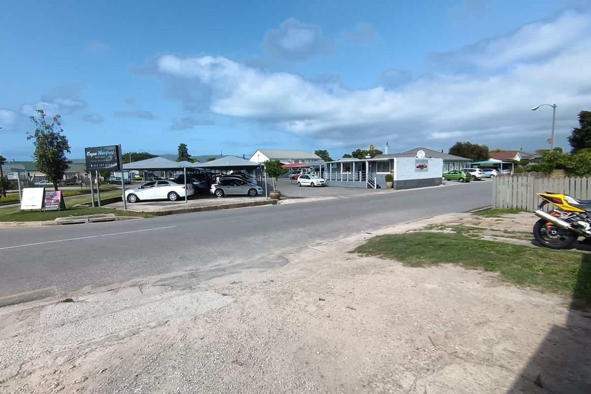 Street view of a commercial property featuring a paved parking area with carports and surrounding fencing.