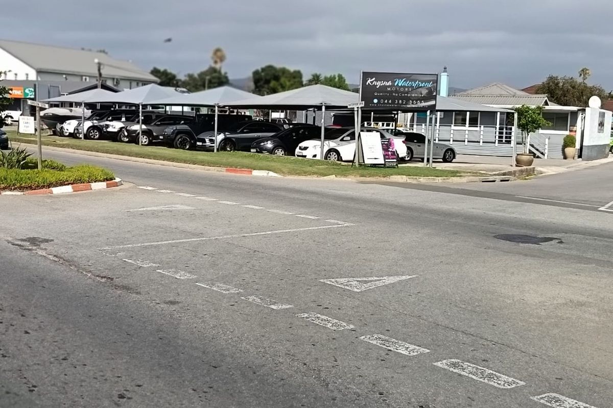 Street view of a commercial car dealership property featuring paved parking areas and shade cloth carports.