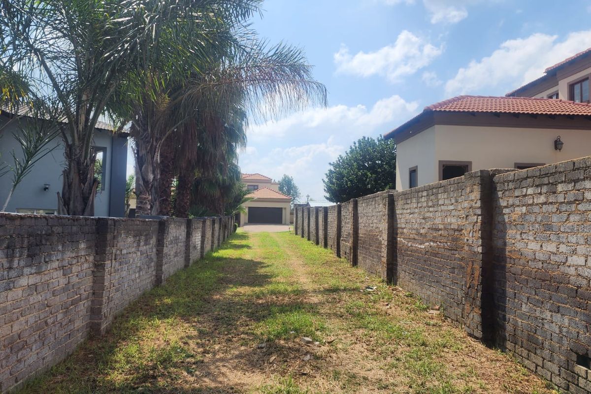 A view of a residential vacant land plot featuring long brick boundary walls and a grass-covered driveway leading towards the rear of the property.