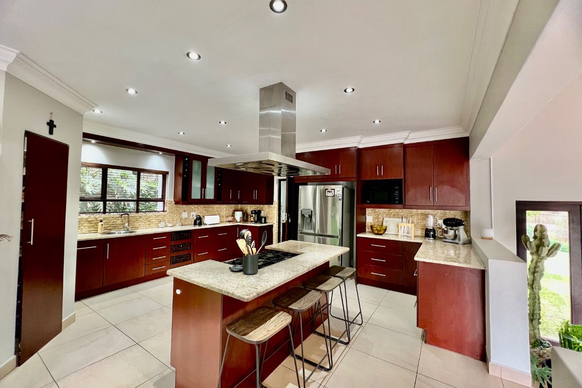 Spacious kitchen featuring dark wood cabinetry, stone countertops, a central island with a gas cooktop, and modern stainless steel appliances.