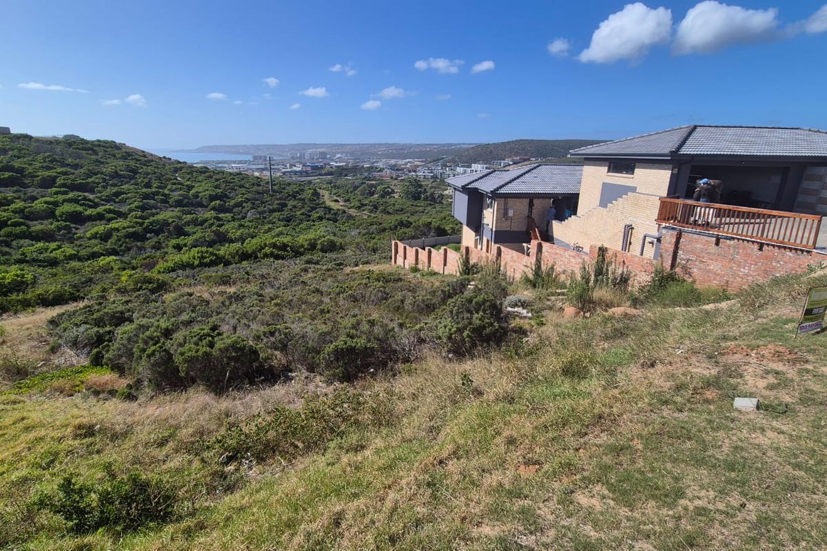 A view of a vacant residential plot featuring natural vegetation, with a neighboring property and distant coastal landscape in the background.
