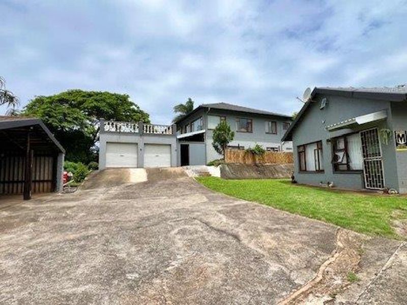 Front view of the property featuring a concrete driveway, double garage, and multi-level residential structures with established garden areas.