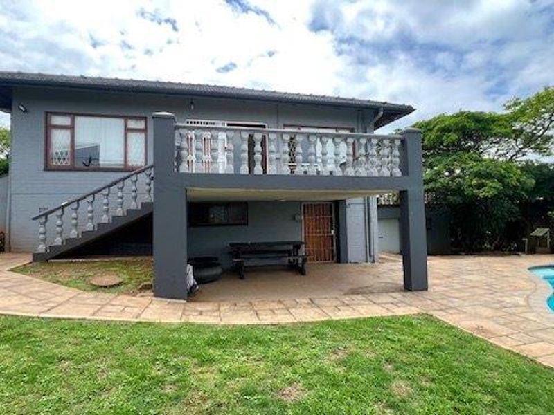 Rear view of the house featuring a raised balcony with concrete balustrades, a covered patio area, and an adjacent swimming pool.