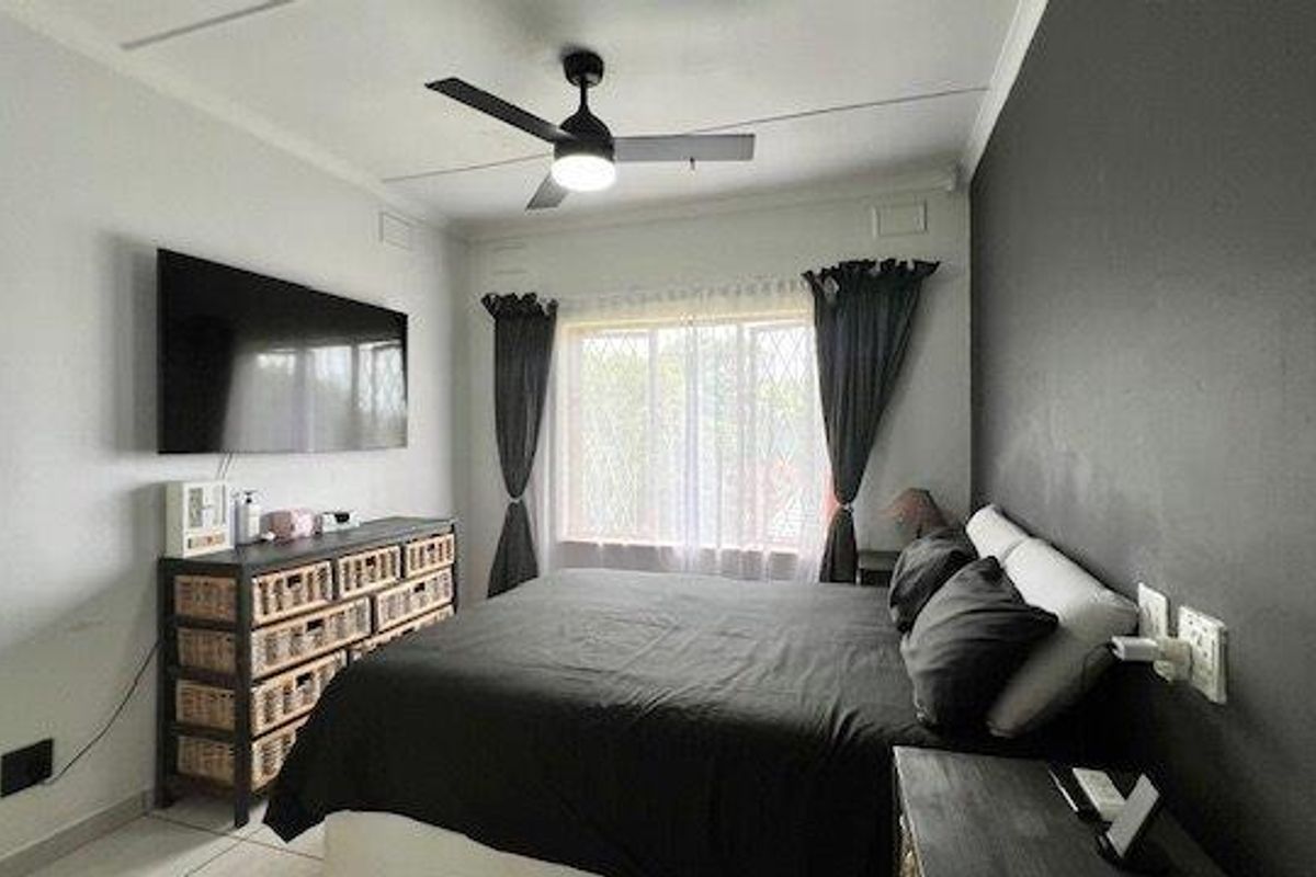 A well-maintained bedroom featuring a ceiling fan, security bars on the window, and a modern dark accent wall.