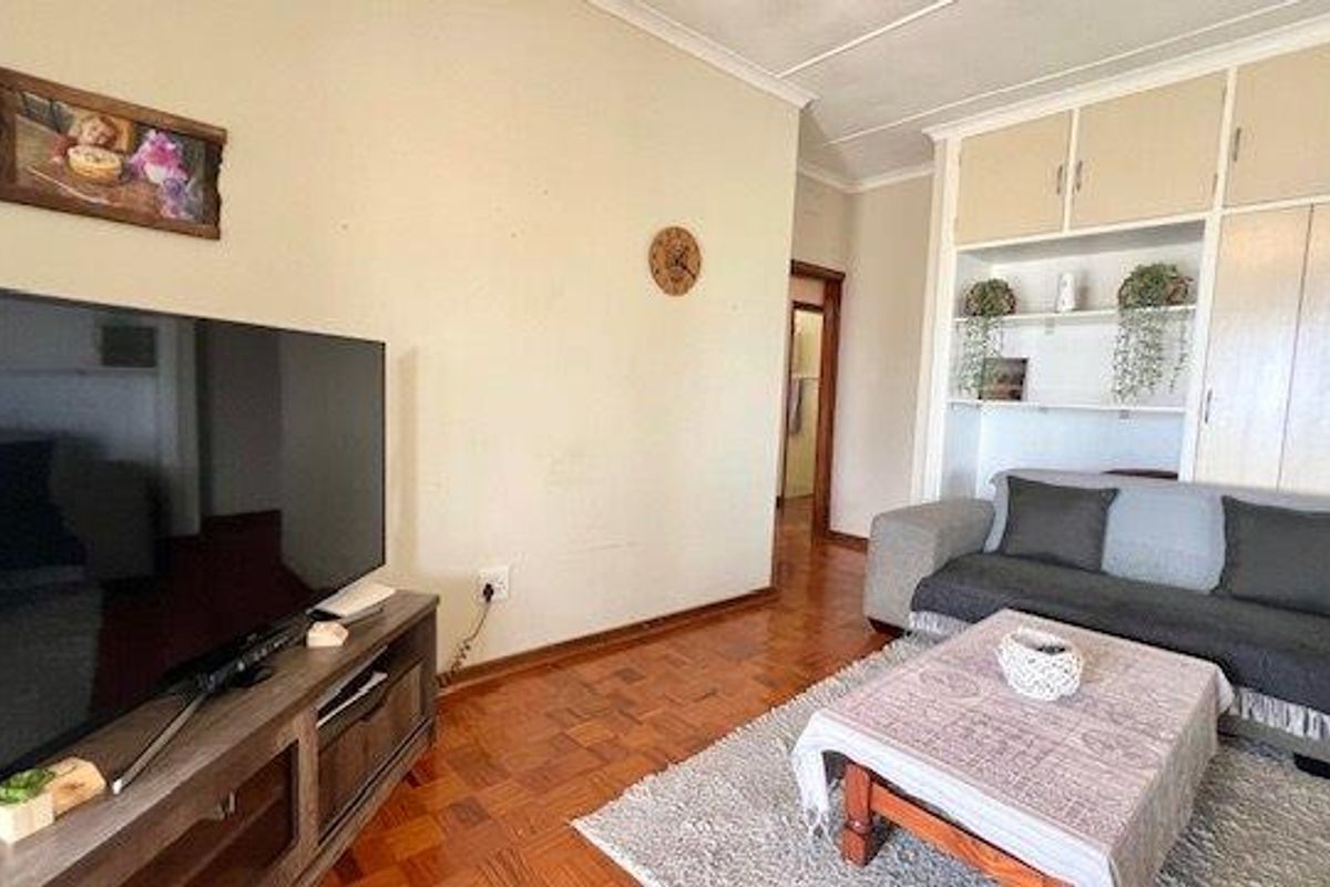 A living room featuring classic parquet flooring, built-in storage cabinetry, and coving, offering a functional space with potential for cosmetic updates.
