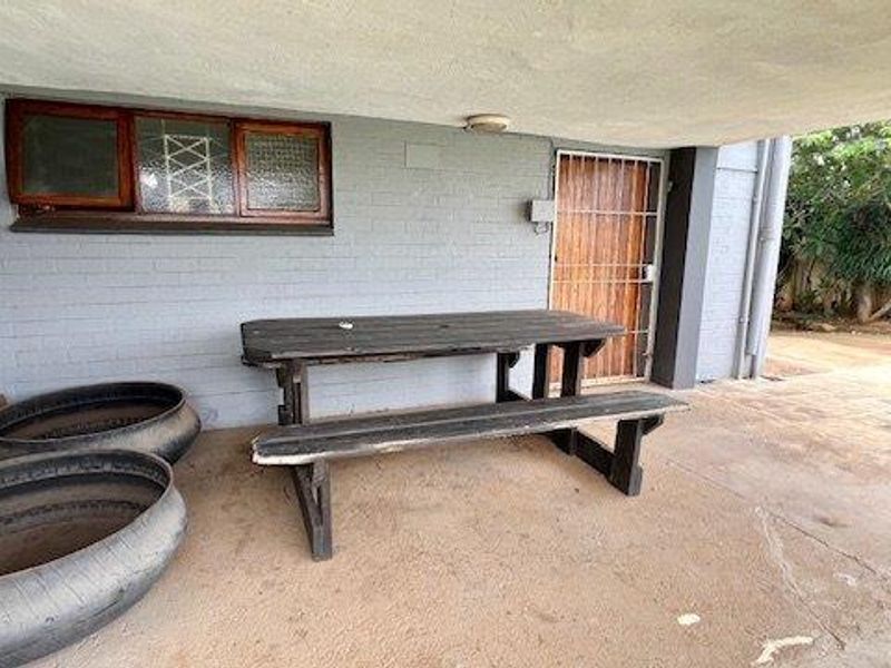 A covered outdoor patio area featuring brick walls, paved flooring, and a security gate, providing a functional space for outdoor relaxation.