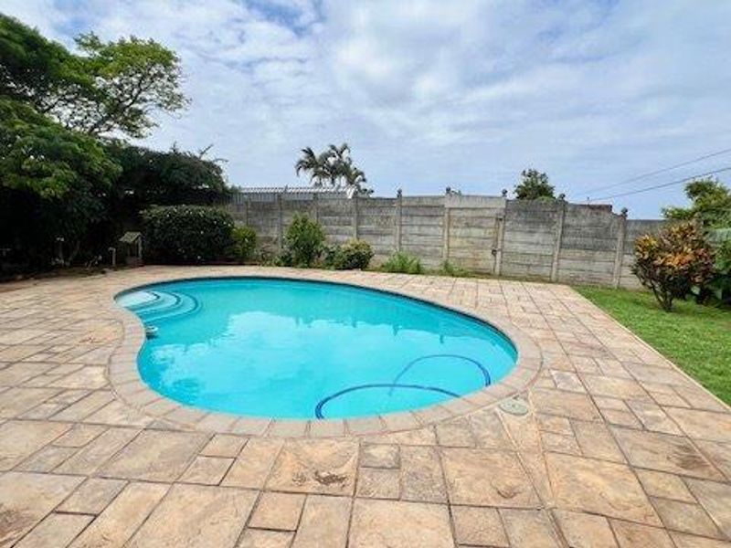 A well-maintained outdoor pool area featuring a kidney-shaped swimming pool, paved surround, and a secure precast concrete boundary wall.