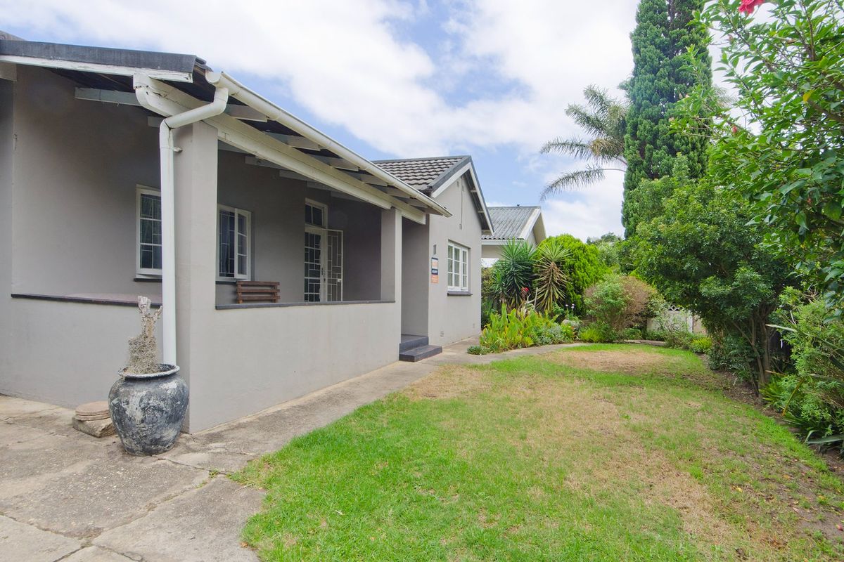 A view of the rear exterior featuring a covered patio, concrete walkway, and a well-established garden area with mature trees and lawn.