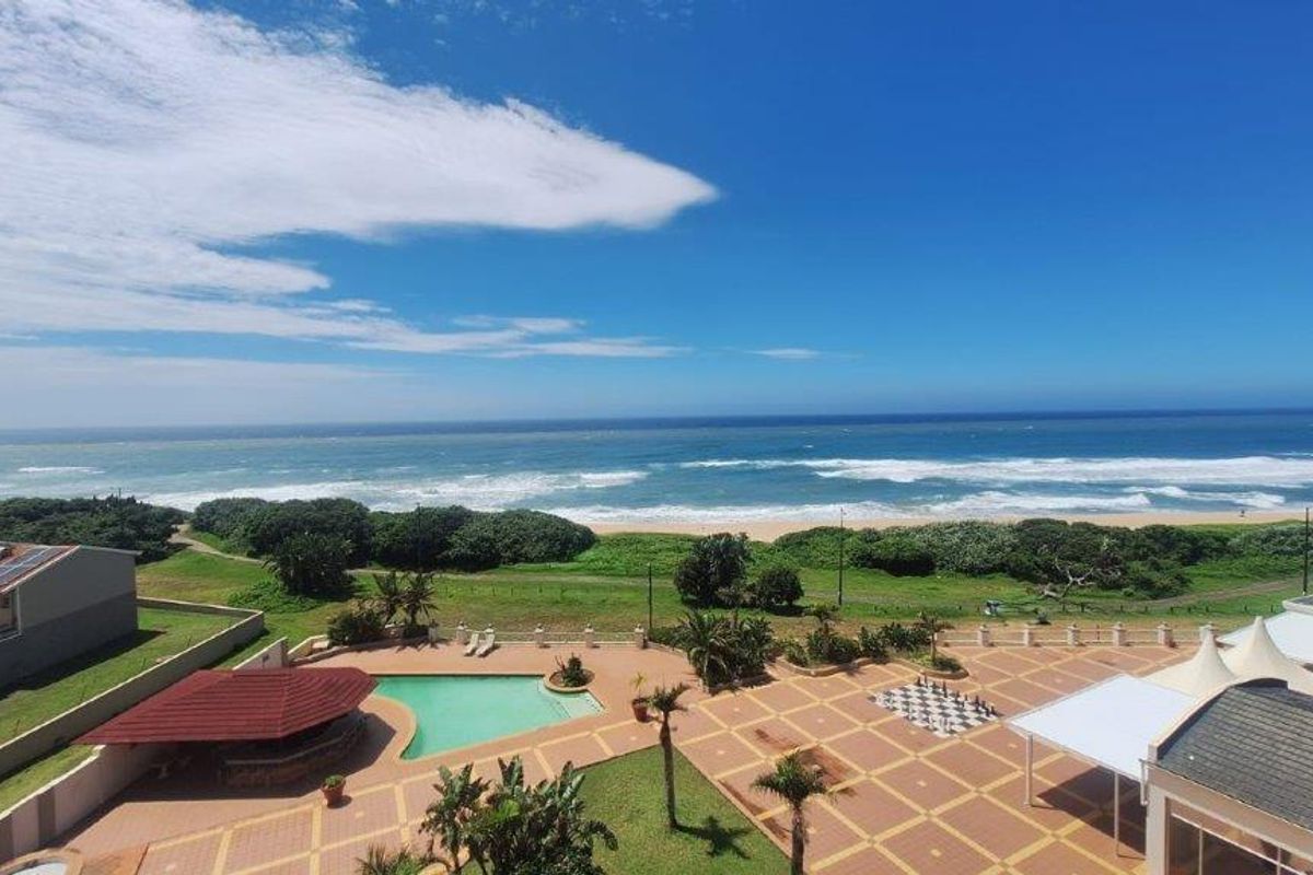 Elevated aerial view of the apartment complex featuring a swimming pool, paved courtyard, and direct ocean views.