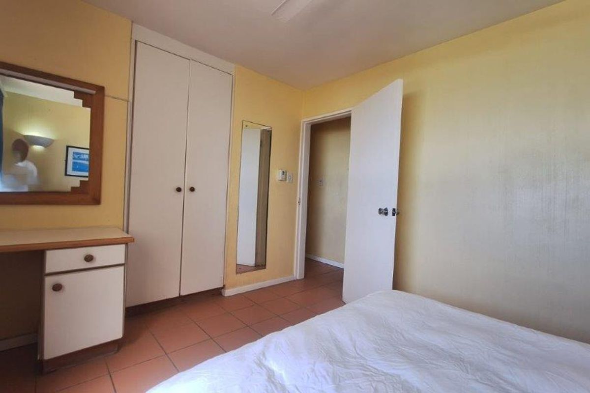 A bedroom featuring built-in cupboards, a vanity unit, and tiled flooring, offering a functional space with potential for cosmetic updates.