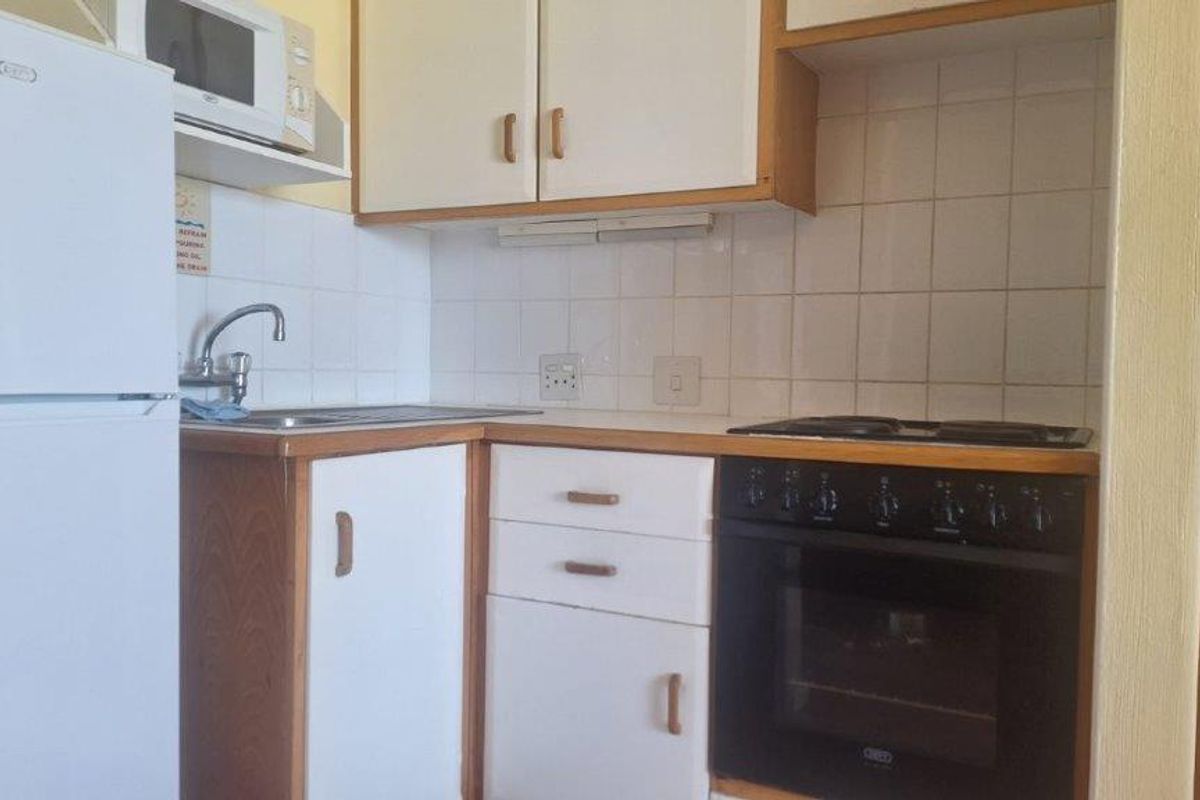 Compact kitchen featuring white cabinetry, a built-in oven and hob, tiled splashback, and a stainless steel sink.