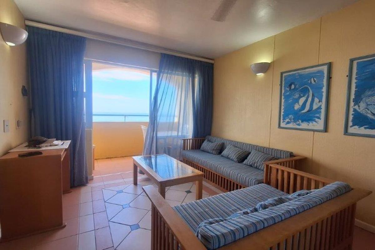 A living room featuring tiled flooring and sliding glass doors that open onto a balcony with ocean views.