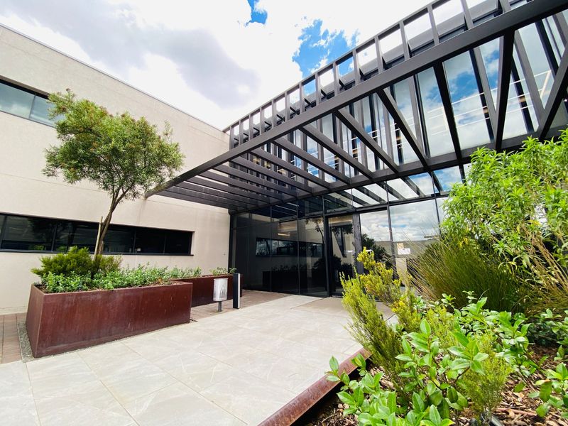 Modern commercial building entrance featuring a striking metal pergola, glass facade, and contemporary corten steel planters in a well-maintained landscaped setting.