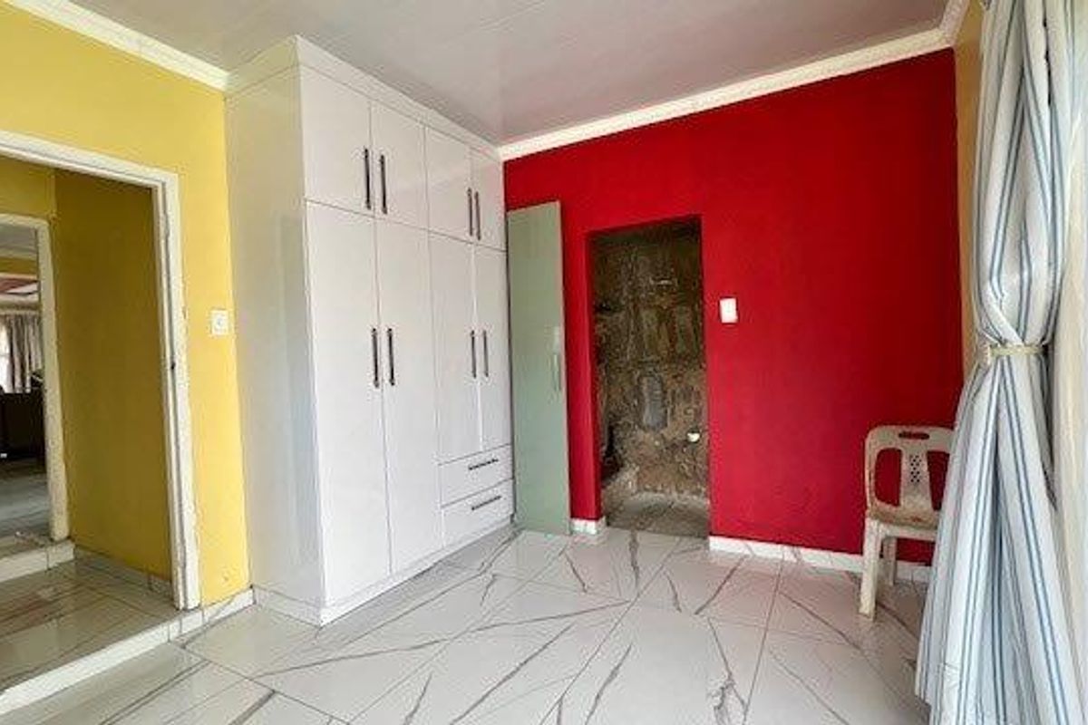 A bedroom featuring white built-in cupboards, modern marble-look tiled flooring, and access to an en-suite bathroom.