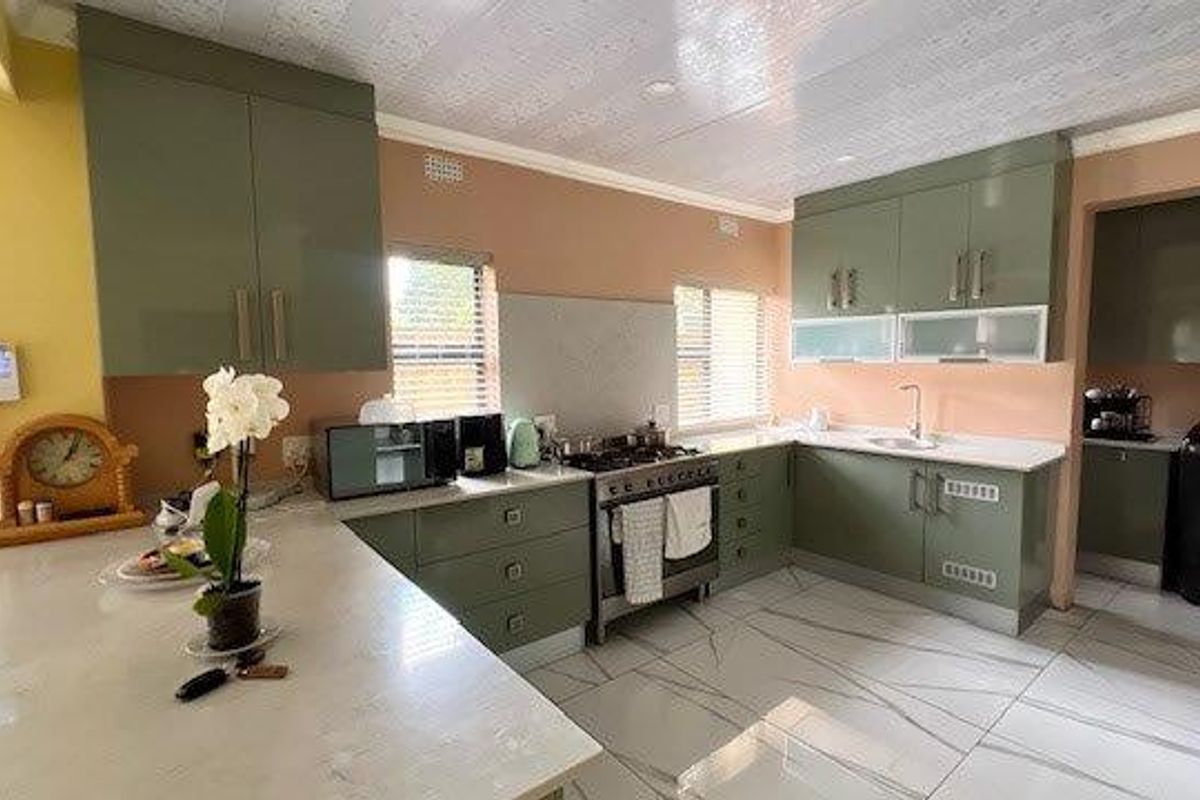 Modern kitchen featuring olive green cabinetry, stone countertops, gas stove, and tiled flooring with a connected scullery area.