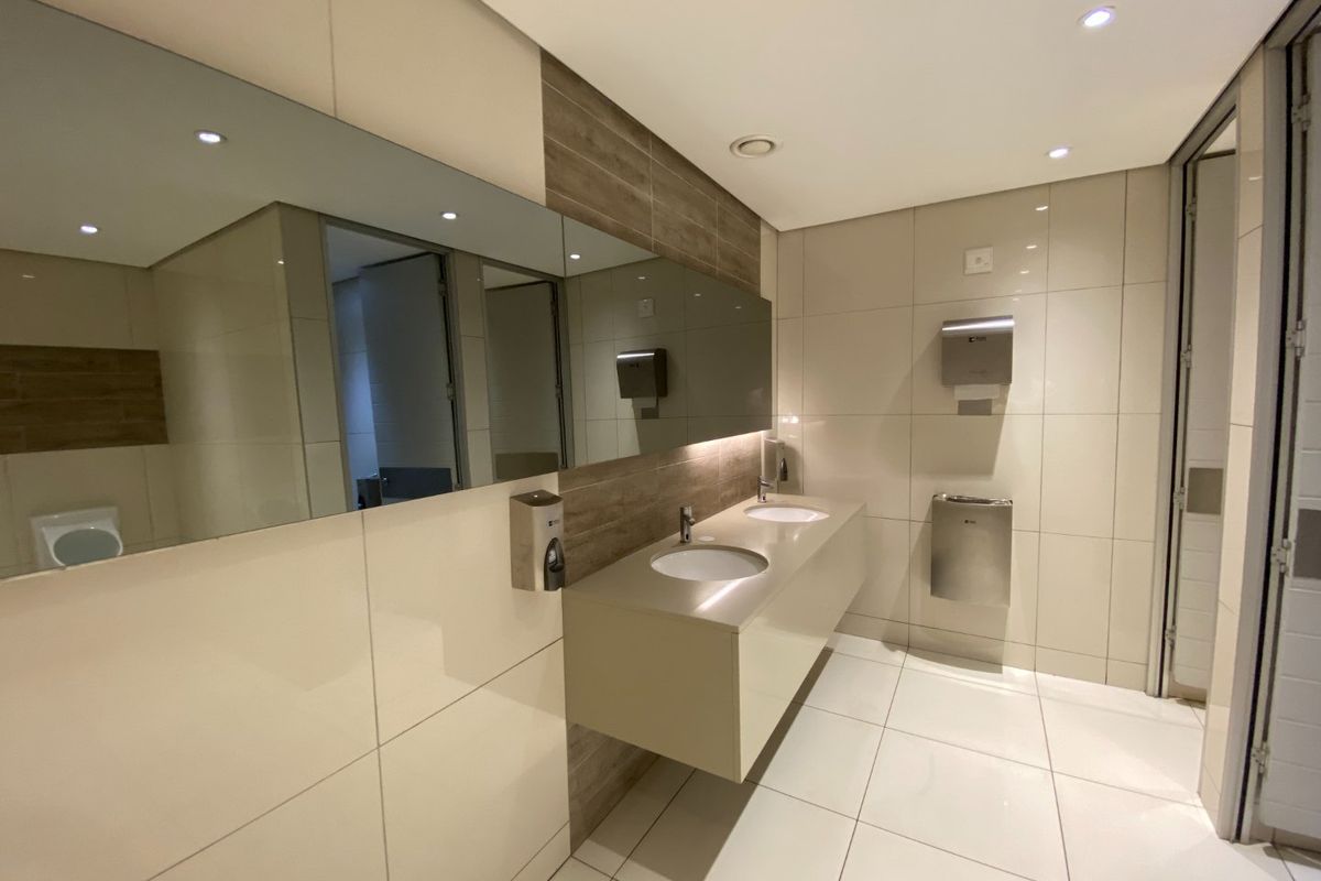 Modern commercial restroom featuring a floating double vanity with integrated sinks, large wall-mounted mirror, and high-quality tiled finishes.