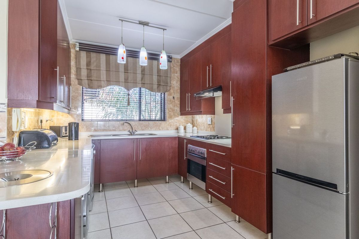 A well-maintained kitchen featuring dark wood cabinetry, stone countertops, tiled flooring, and integrated appliances including a built-in oven and hob.