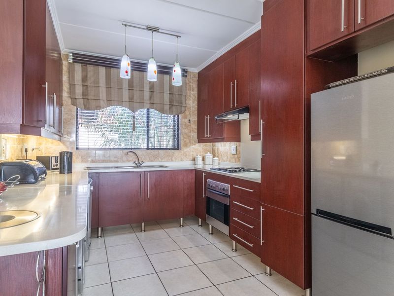 A well-maintained kitchen featuring dark wood cabinetry, stone countertops, tiled flooring, and integrated appliances including a built-in oven and hob.