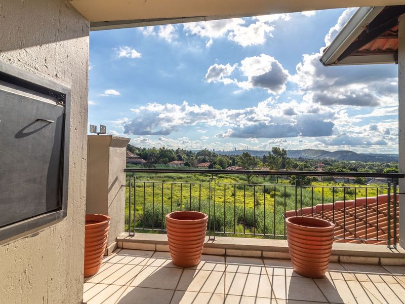 A spacious balcony featuring a built-in braai, tiled flooring, and a metal railing, offering scenic elevated views of the surrounding landscape.