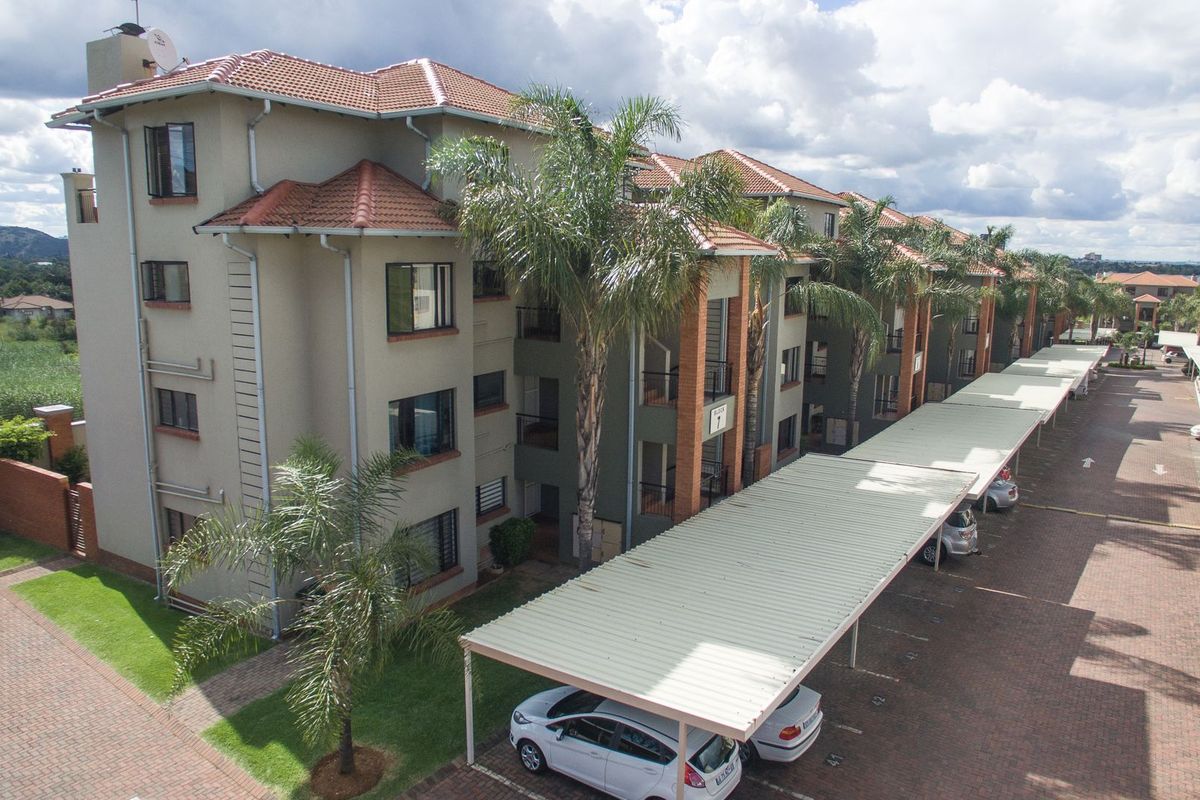 Aerial view of a multi-story apartment complex featuring tiled roofs, covered parking bays, and well-maintained paved driveways and landscaped grounds.