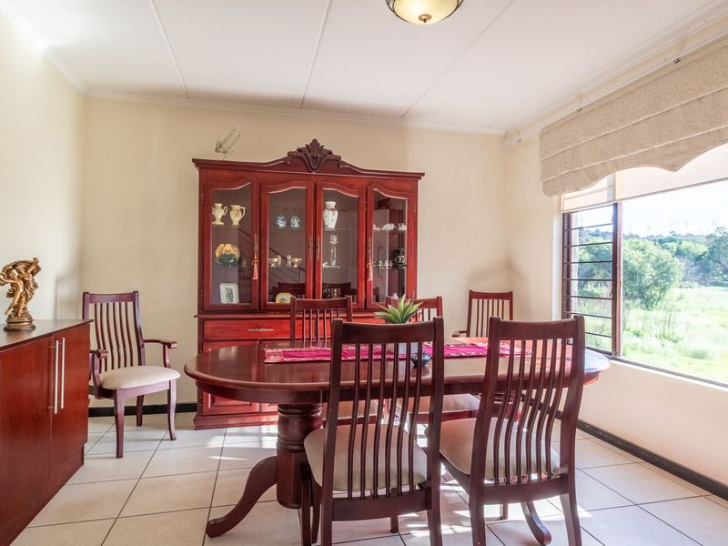 A bright dining room featuring tiled flooring, a large window with a roman blind, and ample space for a dining suite.