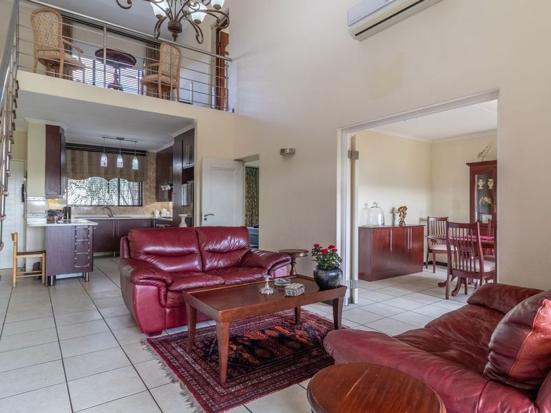 Spacious open-plan living area featuring a mezzanine level, tiled flooring, a modern staircase with stainless steel balustrades, and an adjoining kitchen.