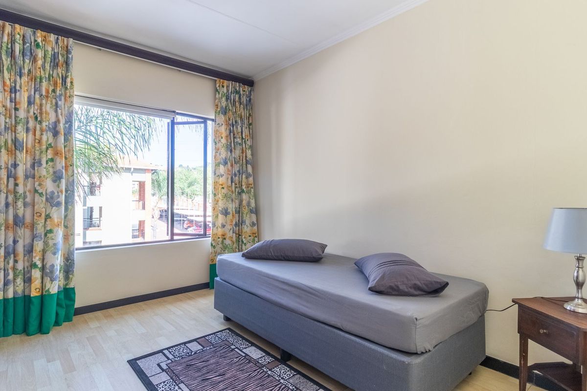 A functional bedroom featuring laminate flooring, a large window providing natural light, and a built-in wardrobe for storage.