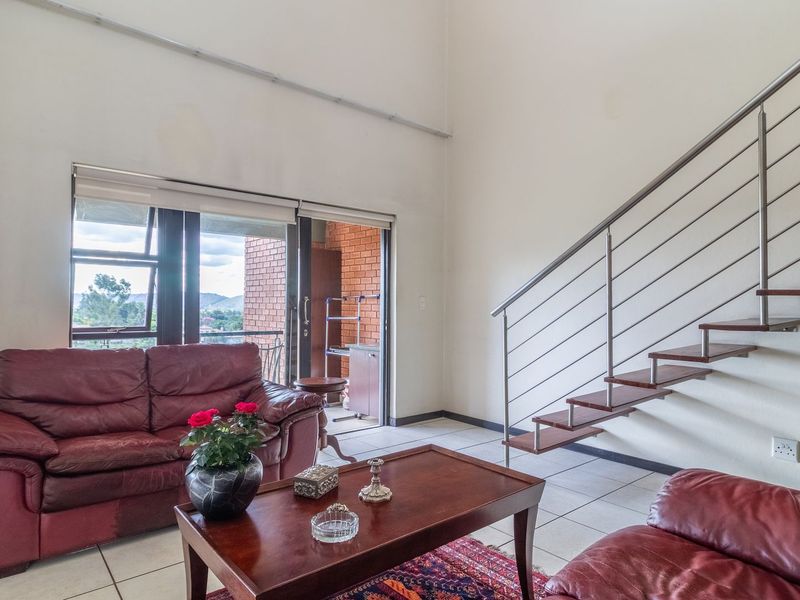 Spacious living area featuring high vaulted ceilings, tiled flooring, and a modern floating staircase with stainless steel railings, leading to an outdoor balcony.