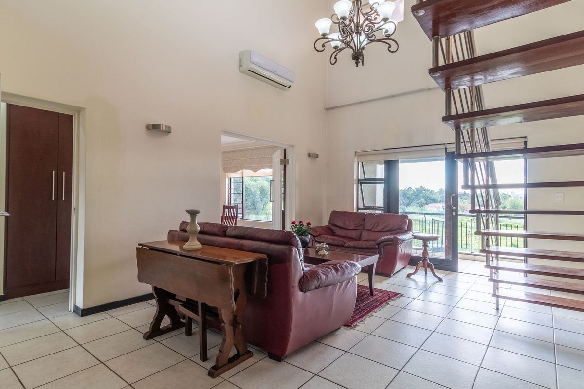 Spacious living area featuring high ceilings, an open-tread staircase, tiled flooring, and direct access to a balcony through sliding glass doors.