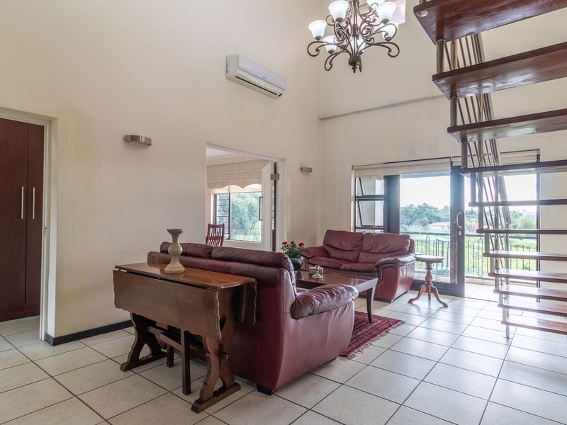 Spacious living area featuring high ceilings, an open-tread staircase, tiled flooring, and direct access to a balcony through sliding glass doors.