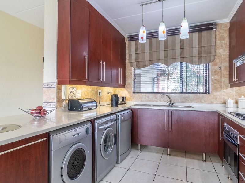 A functional kitchen featuring dark wood cabinetry, stone countertops, integrated appliances, and a tiled backsplash, offering a practical layout for daily cooking and laundry tasks.