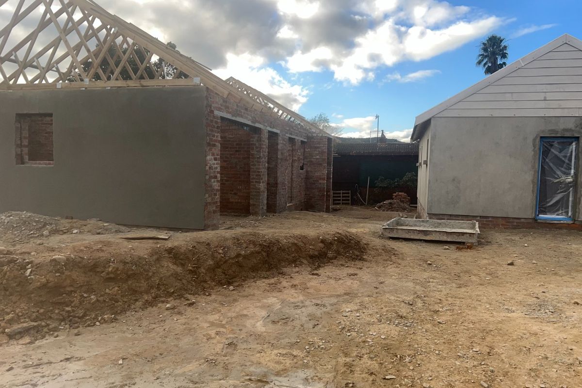 A construction site view showing the rear of a property under development with exposed timber roof trusses and unfinished plastered brick walls.