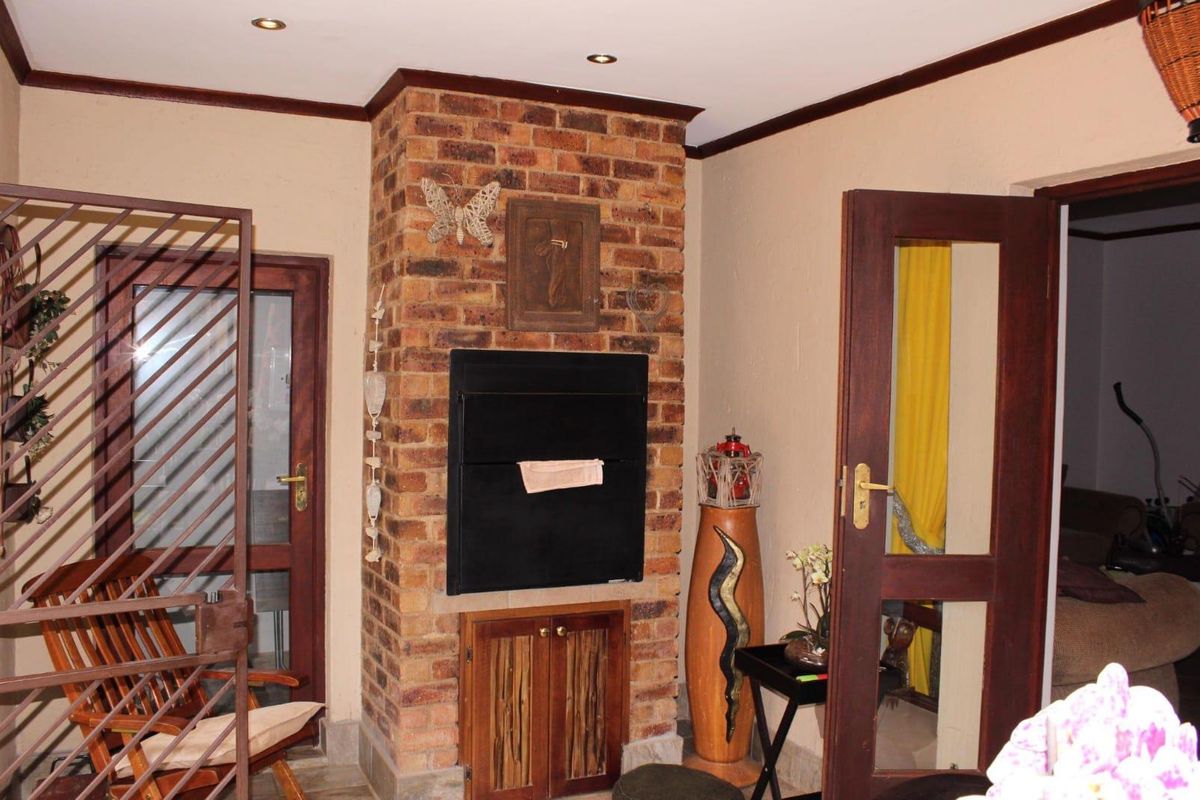 A living area featuring a prominent face-brick fireplace with a built-in hearth and wooden cabinetry, flanked by timber-framed glass doors.