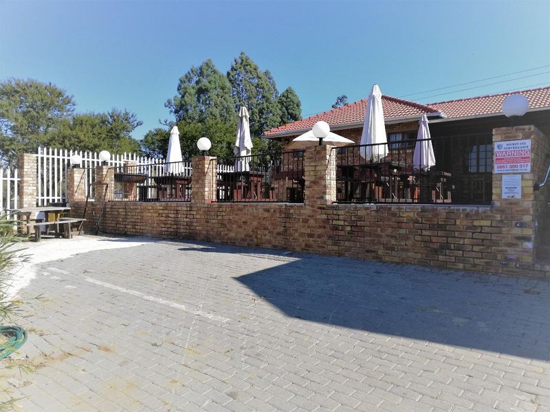 An outdoor patio area featuring a brick boundary wall, metal security fencing, and paved driveway access, suitable for outdoor entertainment.