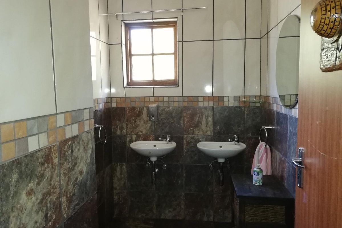 A bathroom featuring dual wall-mounted washbasins, decorative tiled walls, and a small casement window.