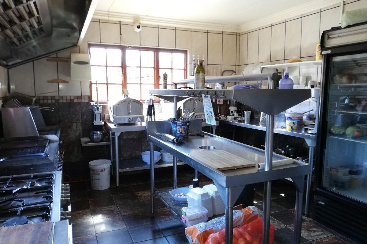 A functional commercial-style kitchen featuring stainless steel prep surfaces, a gas stove, an extractor hood, and tiled finishes throughout.