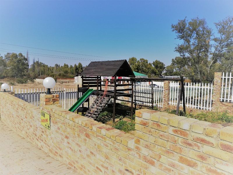 Outdoor garden area featuring a brick boundary wall, white metal fencing, and a timber playground structure.