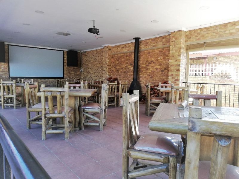 Spacious covered patio featuring exposed brick walls, tiled flooring, a built-in fireplace, and a projector screen, ideal for outdoor entertainment.