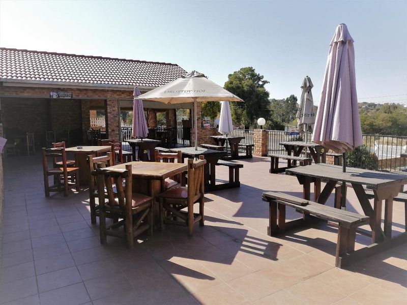 A spacious outdoor patio area featuring tiled flooring, brick structural pillars, and a covered section, suitable for outdoor dining and entertainment.