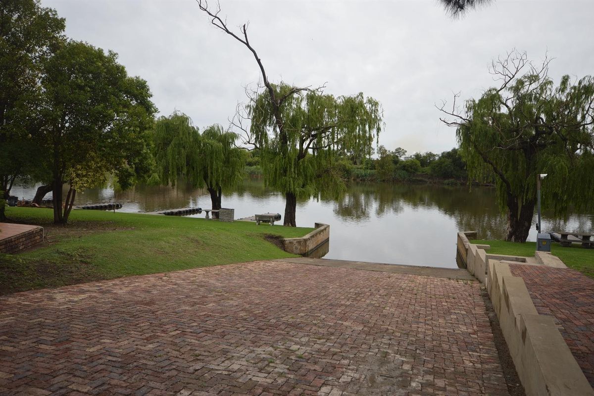 A scenic view of the riverfront featuring a paved boat ramp, manicured lawn, and mature willow trees along the water's edge.