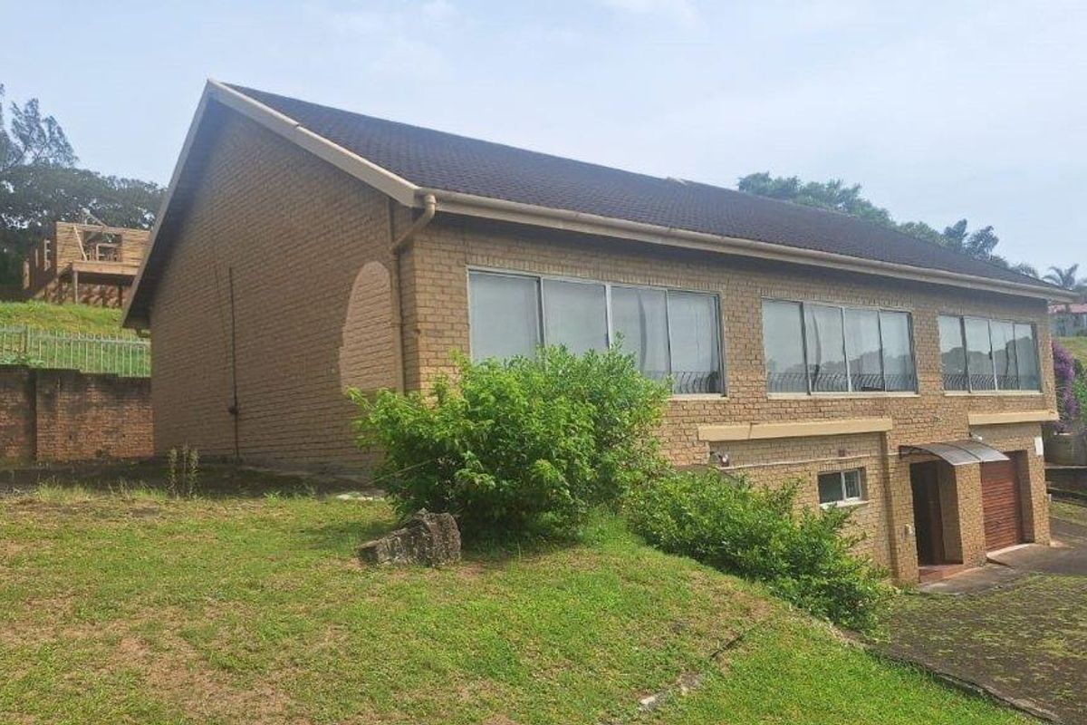 Rear view of a double-story brick house featuring large sliding windows, a tiled roof, and an attached garage with a concrete driveway.