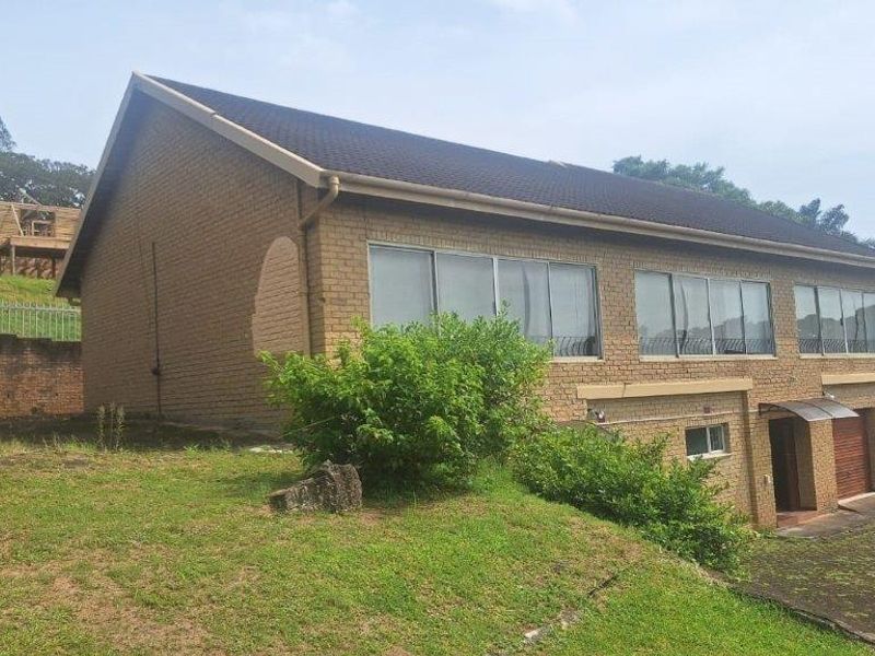 Rear view of a double-story brick house featuring large sliding windows, a tiled roof, and an attached garage with a concrete driveway.