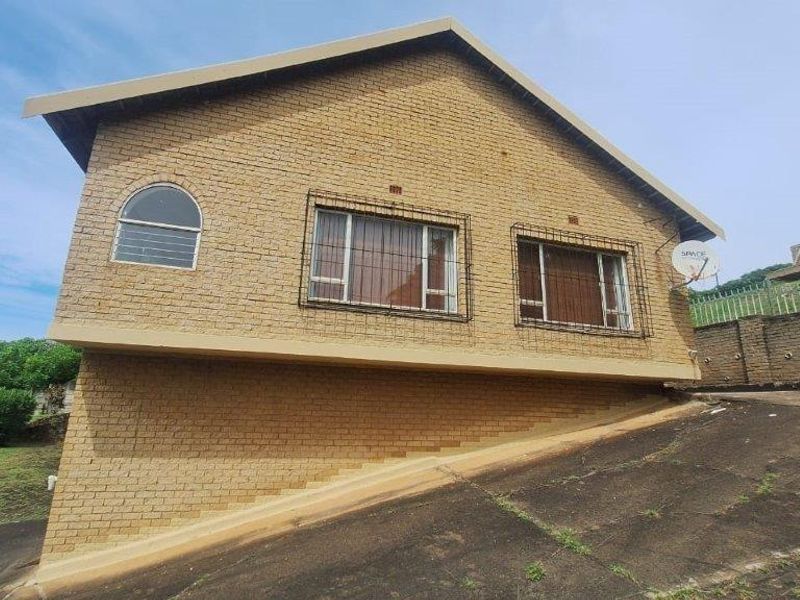 A view of the front elevation of a face brick house featuring security bars on windows and a sloped concrete driveway.